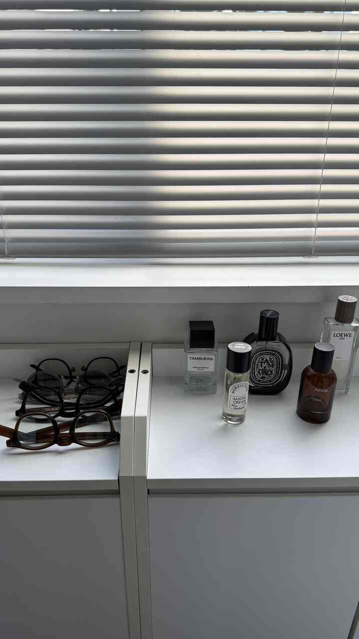 白と黒のトーンの玄関、収納キャビネットに整然と並べられたメガネと香水が置かれた清潔感ある空間