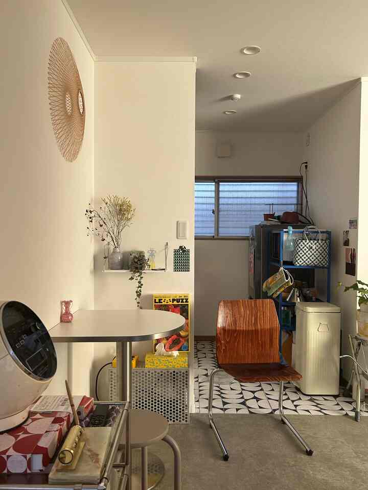 白を基調とした小さなリビングとキッチン、木製の椅子と丸いサイドテーブルが配置された自然で落ち着いた雰囲気のあるインテリア