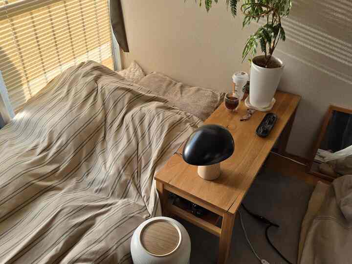 ベージュと木目調の寝室、ストライプ柄の掛け布団カバーとナイトテーブルのテーブルランプが配置された雰囲気のあるインテリア