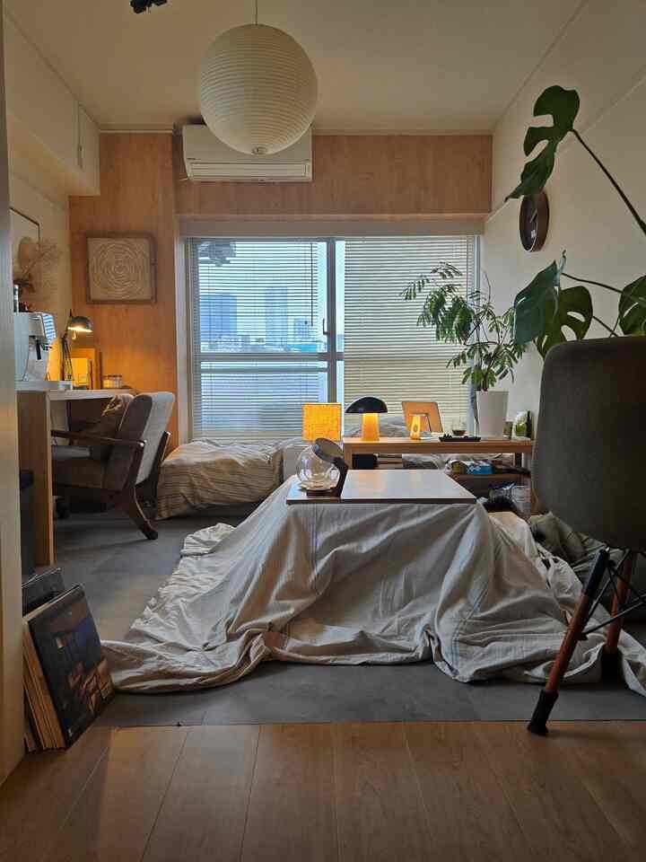 ウッドトーンの壁とグレーの床が調和した、こたつが中央に配置された一人暮らしの寝室の印象的な空間