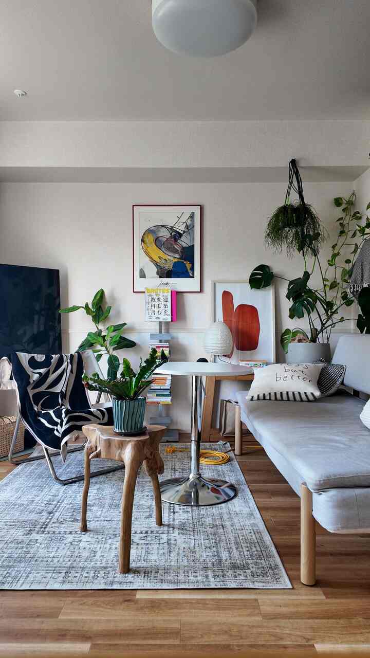 ナチュラルな木目調の床にライトグレーのソファ、植物と額縁が配置されたカフェ風のリビング