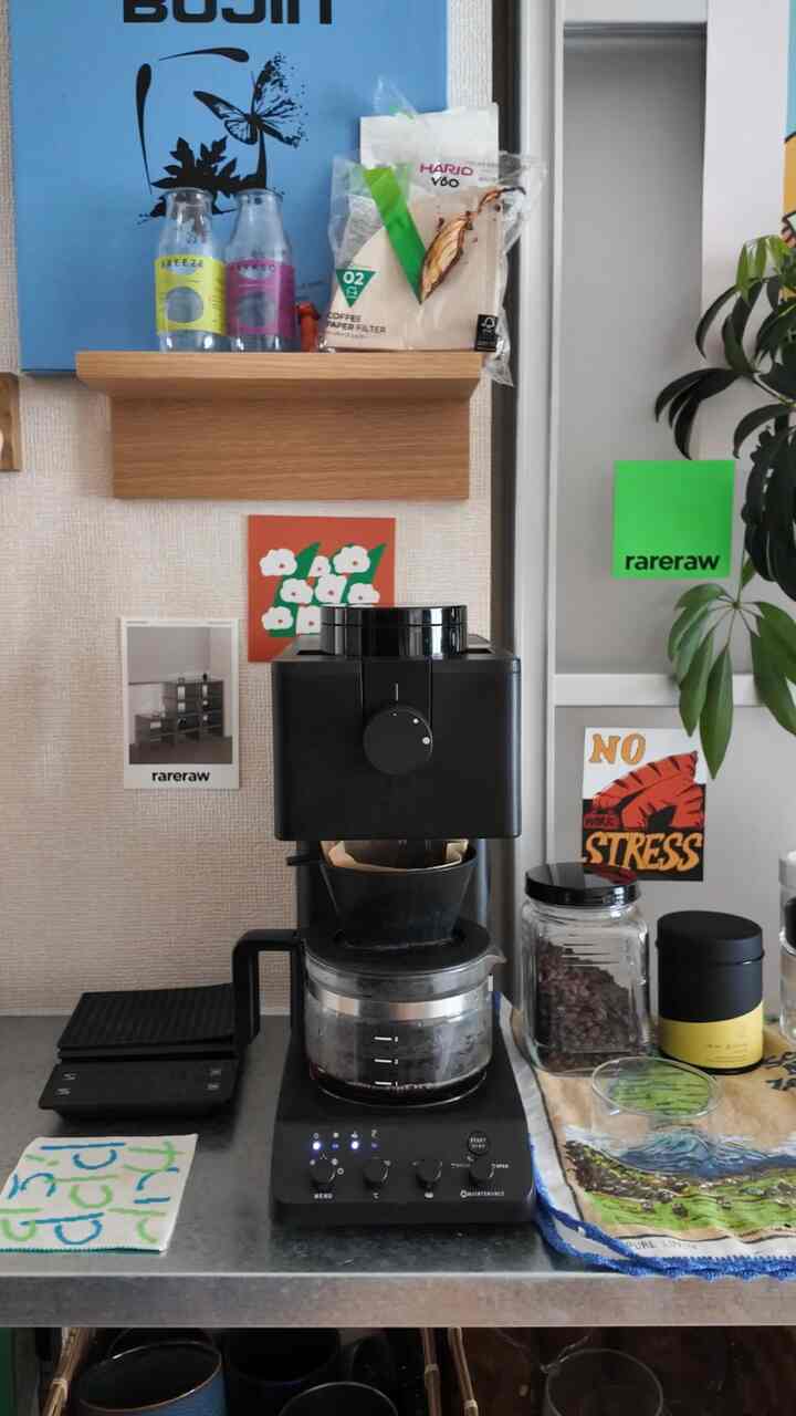 ナチュラルカラーのキッチン空間に、黒い全自動コーヒーメーカーと木製の棚、コーヒー用品が配置された雰囲気のあるおうちカフェ