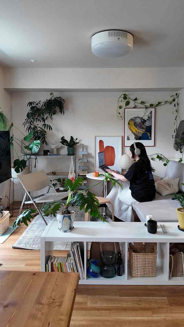 ナチュラルな木目調とグリーンプラントが調和する9畳のリビング、ソファと本棚が配置された落ち着いたホームオフィス空間