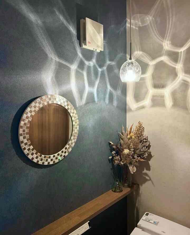 ブルーの壁と丸い鏡、ペンダントライトが配置されたシンプルでナチュラルな雰囲気のバスルーム