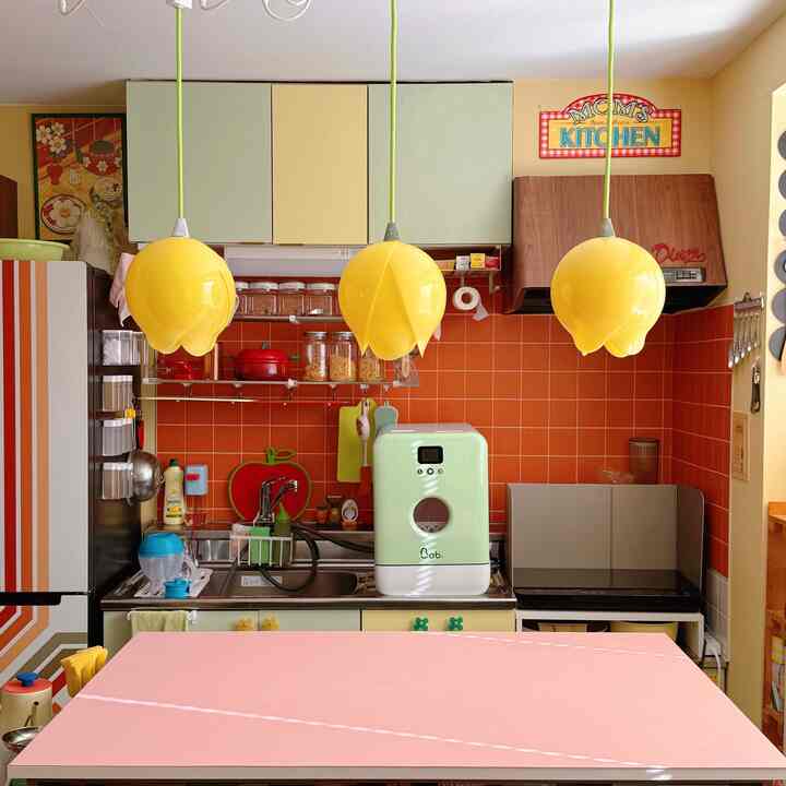 オレンジ色のタイル壁と黄色のチューリップペンダントライトが配置された印象的なキッチン