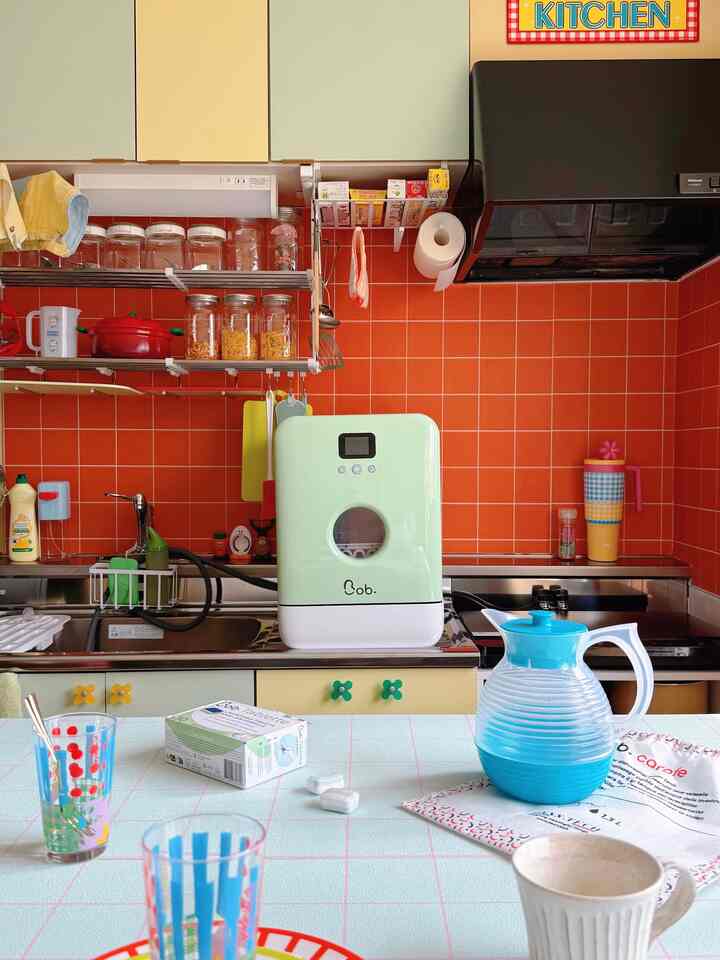 ミントグリーンとオレンジのタイル壁が特徴のキッチン、かわいいレトロな食洗機と整理された調理器具が配置された雰囲気のあるインテリア