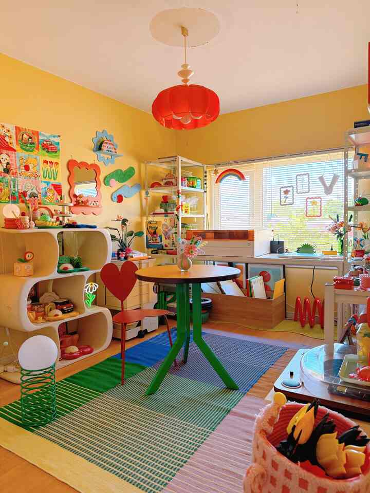 黄色い壁のホームオフィスと子供の遊び場、カラフルな装飾と中央の丸テーブルが配置された印象的な空間