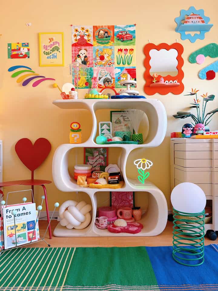 黄色の壁と白い曲線のオープンシェルフがある子供部屋、多彩なおもちゃと装飾品が並ぶ