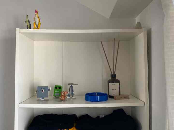 ホワイトトーンの寝室の棚、トムとジェリーのオブジェとディフューザーが配置された印象的な空間