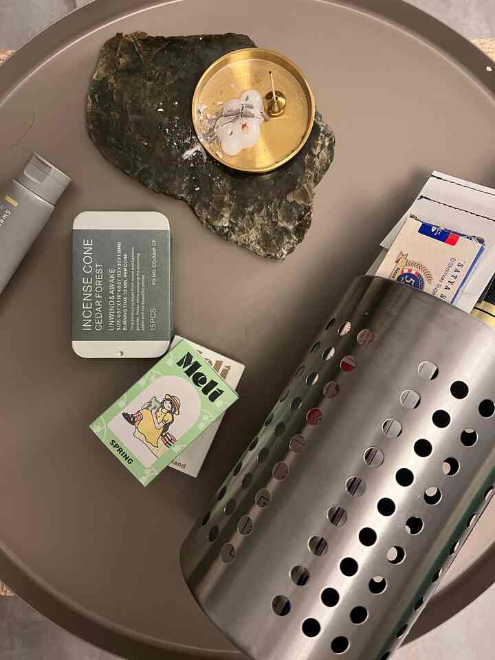 ベージュトーンの丸いトレイの上にステンレスの調理器具ホルダーと真鍮のお香ホルダーが置かれたシンプルなキッチン小物の配置