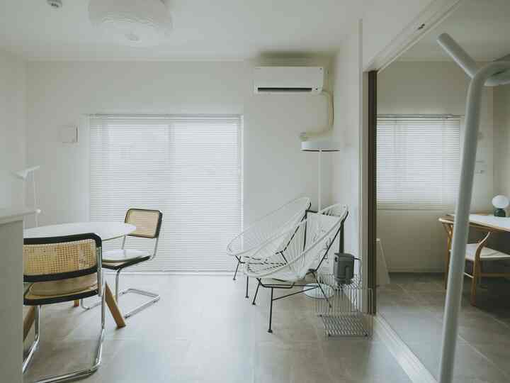 白を基調としたモダンなリビングとダイニング、ブラインドとラタンチェアが配置されたシンプルな空間