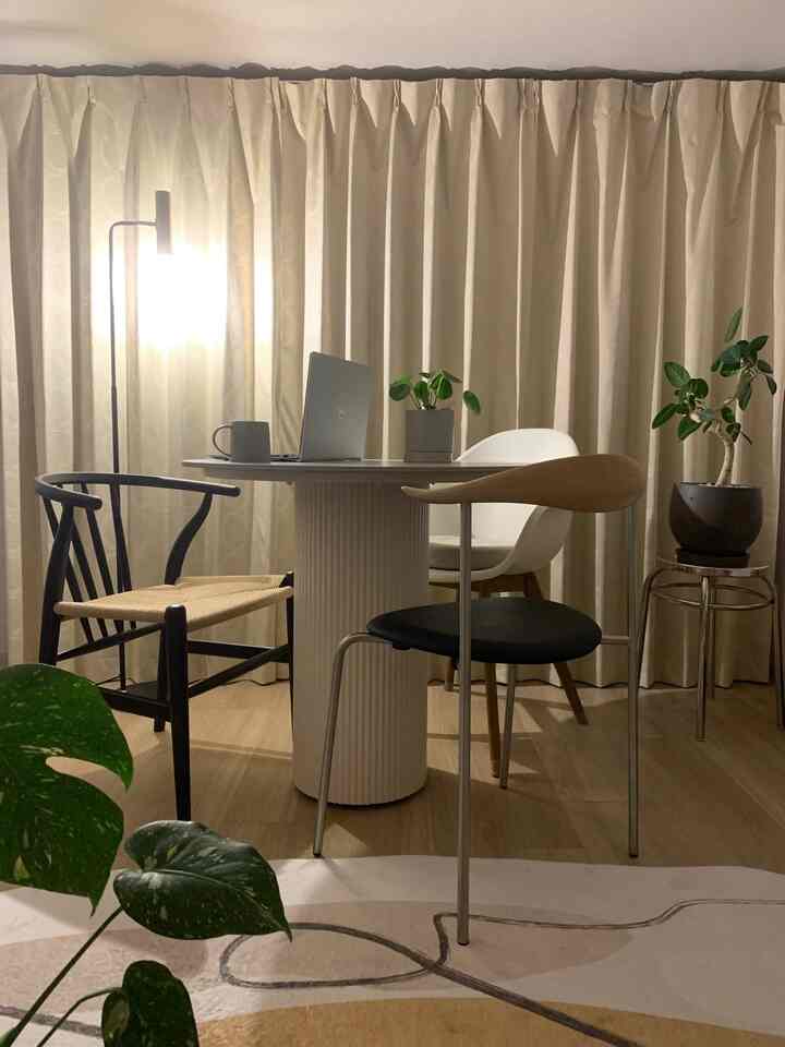 暖かいナチュラルカラーのダイニング、中央に食卓と様々な椅子が並び、フロアランプと植物が調和する空間