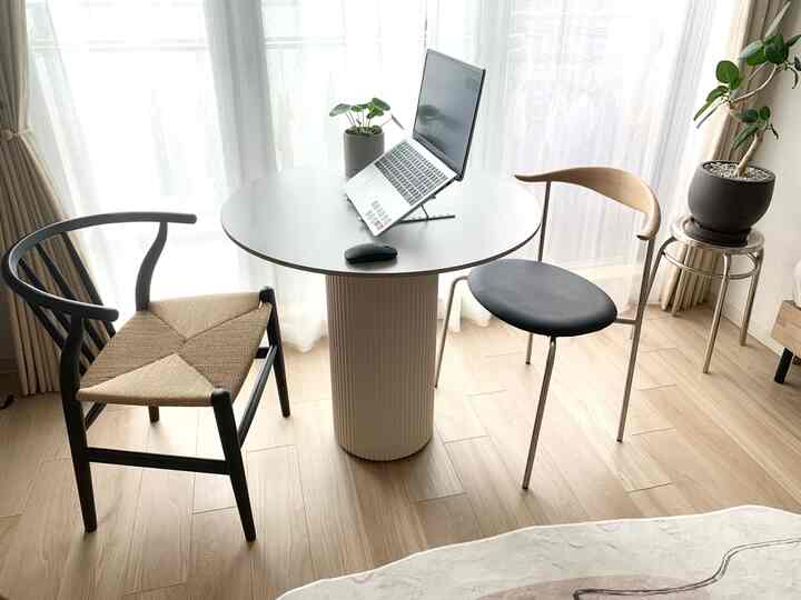 ナチュラルトーンのワンルームダイニングスペース、丸テーブルと2脚の椅子が配置され、ノートパソコンと植物で清潔感のある雰囲気