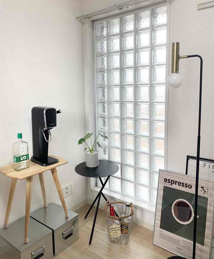 透明なガラスブロックのあるカフェ風の小さなコーナー、木製スツールとフロアランプが配置された落ち着いた空間