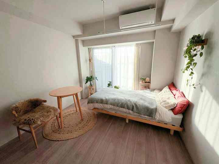 白と木目調のナチュラルなワンルーム寝室、丸テーブルと椅子が配置されたシンプルで落ち着いたインテリア