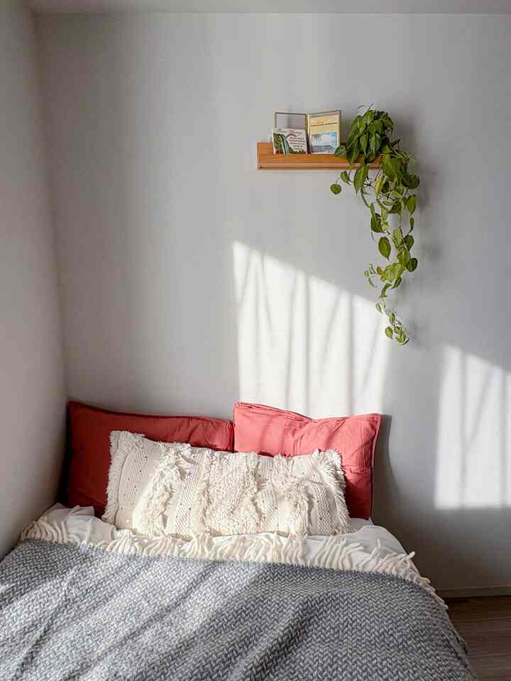 白とグレーのトーンの寝室コーナー、ベージュのクッションと吊り下げ植物が配置されたシンプルで自然な雰囲気のインテリア