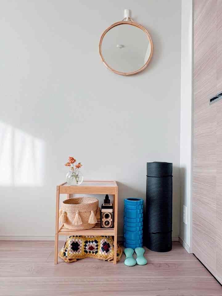 ナチュラルな色調の寝室のコーナー、ラタンの丸い鏡と木製のナイトテーブル、運動用品が配置された落ち着いた空間