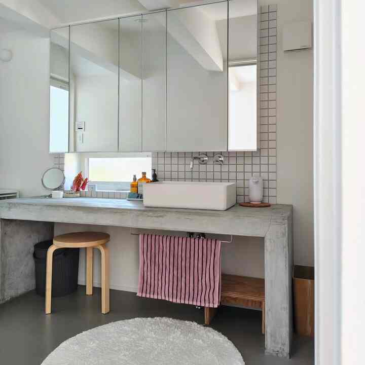 白とグレーのモダンなパウダールーム、ナチュラルな木製スツールと大きな鏡収納が配置された印象的な空間