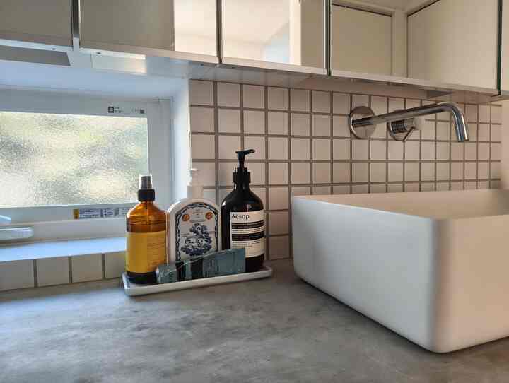 白とグレーのトーンのバスルーム、無印良品のトレイに洗浄剤が整然と並べられたモダンな雰囲気のインテリア