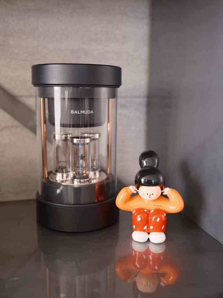 黒とオレンジのトーンの小さな棚スペースにBALMUDAのワイヤレススピーカーと装飾用フィギュアが置かれた雰囲気のあるインテリア