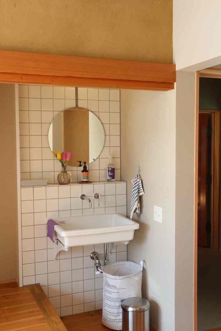 ナチュラルトーンのパウダールーム、タイル張りの壁と丸い鏡、木目調の床とシンプルな洗面台が配置された雰囲気のあるインテリア