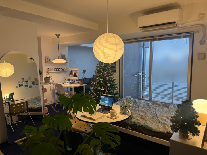 ネイビーのカーペットと白い壁が調和する一人暮らしの寝室、デスクやソファ、クリスマスツリーがある雰囲気のあるインテリア