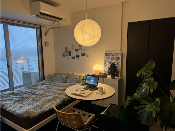 白を基調としたワンルーム寝室、左手にシングルベッド、右手にテーブルと椅子が配置された自然感あふれるインテリア