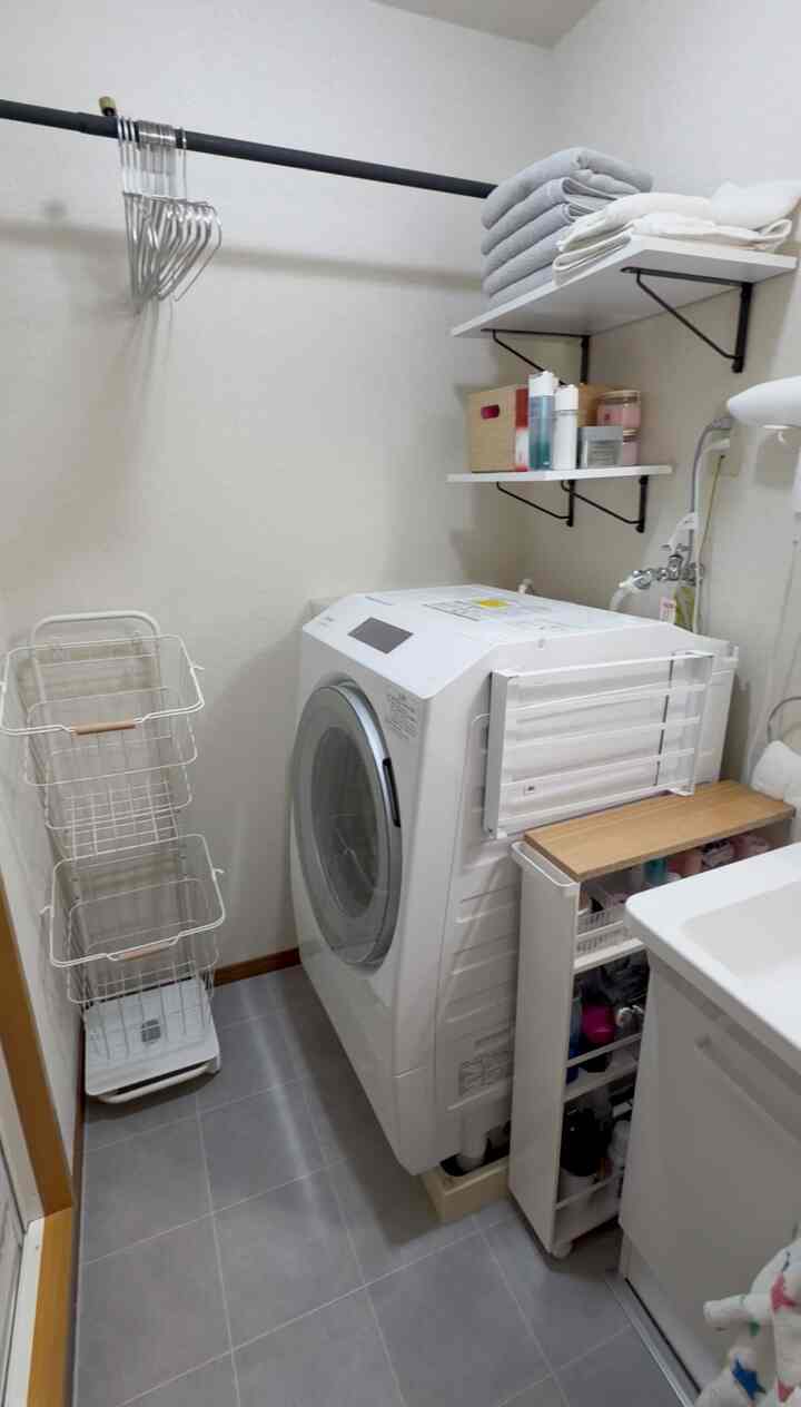 白とグレーの色調が特徴の狭く縦長なランドリールーム、洗濯機と収納棚、ハンガーラックが配置された整頓された空間