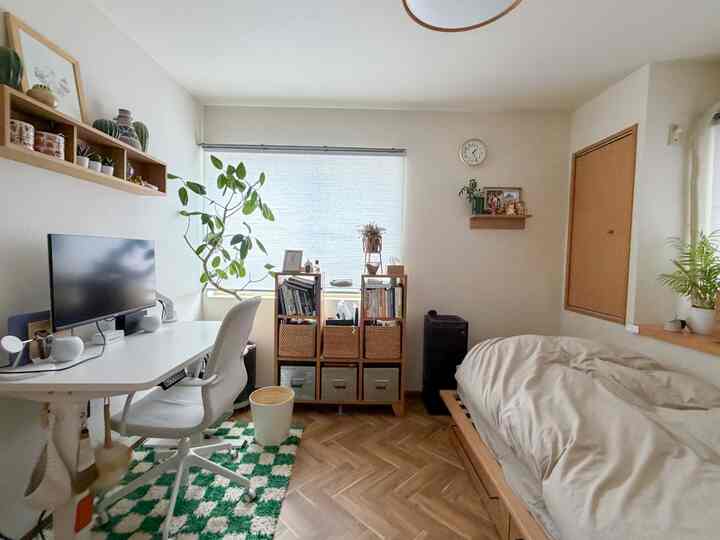 白い壁と木目調のベッドフレーム、デスク、植物が配置されたナチュラルモダンな6畳の寝室兼ホームオフィス