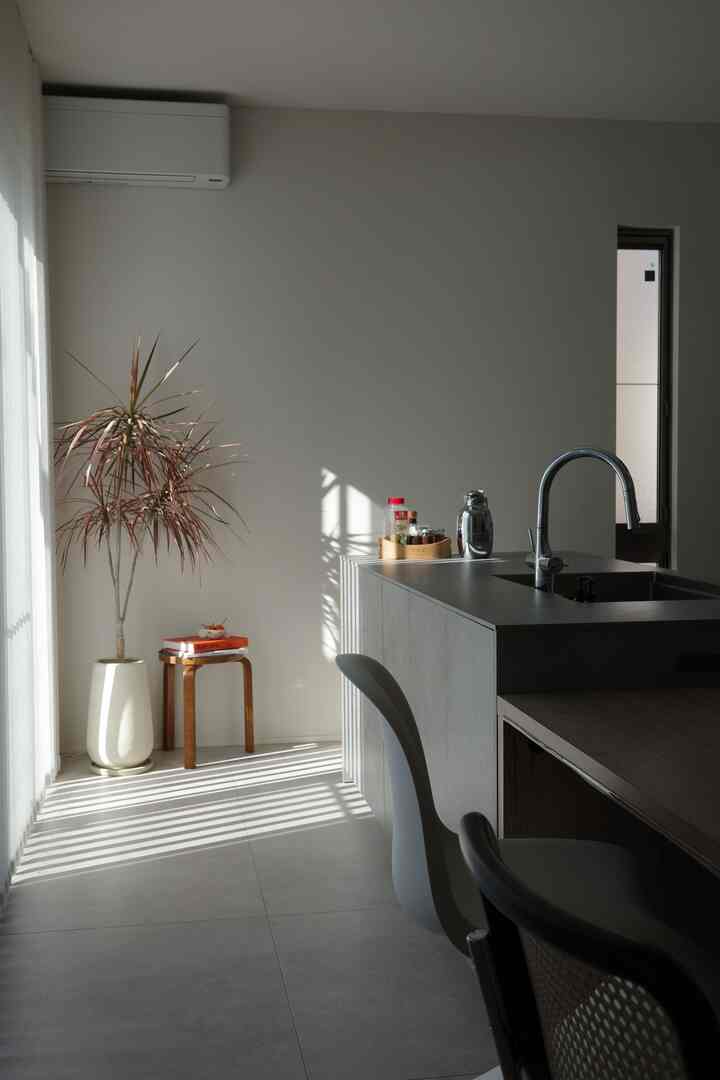 白とナチュラルカラーのキッチンとリビングの空間、シンプルなスツールとダイニングチェアが配置された清潔感のあるインテリア