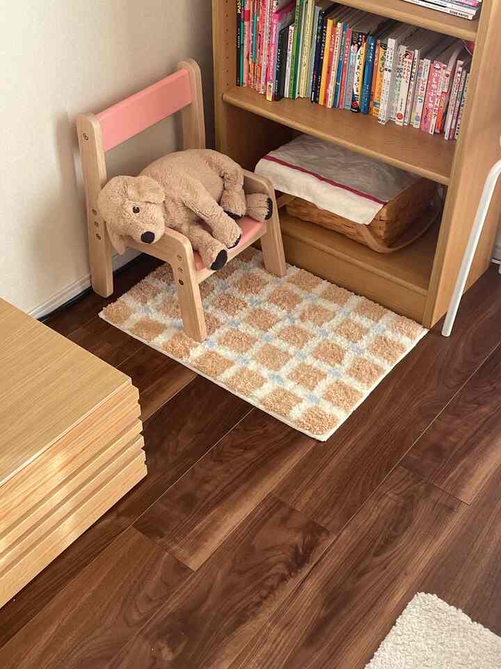 ナチュラルな木目調の床と本棚がある子供部屋の一角に、ピンクの子供椅子とぬいぐるみの犬が置かれた雰囲気のある空間
