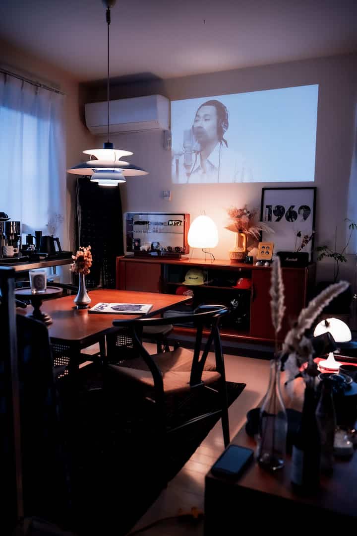 ウッドトーンのナチュラルな色調のリビング兼ダイニングルーム、プロジェクターとペンダントライトが配置されたモダンなインテリア