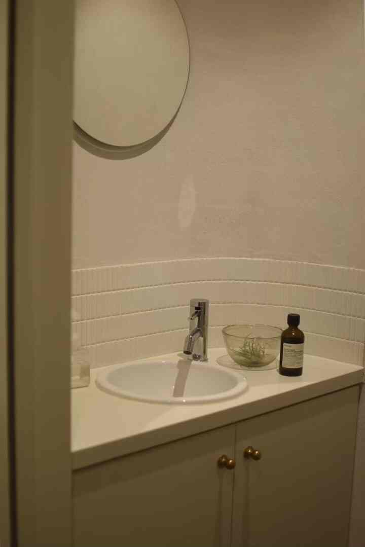ベージュと白を基調としたトイレの洗面スペース、丸い鏡とシンプルな収納が配置された落ち着いたインテリア