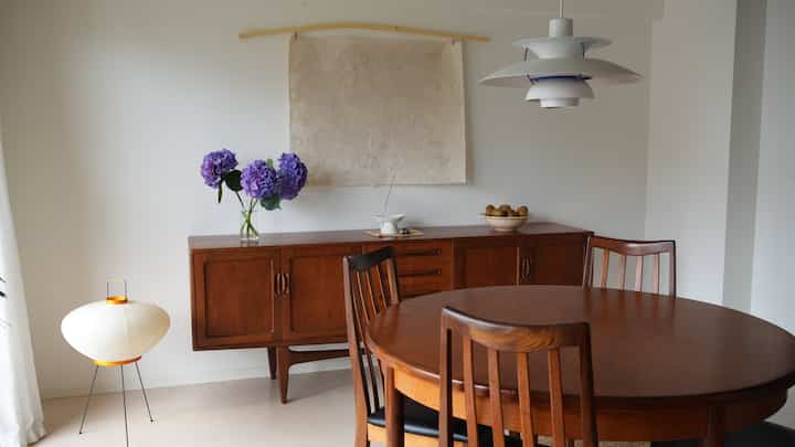 白い壁とブラウンの木製家具が配置されたミッドセンチュリーモダンなダイニングルーム、落ち着いた照明が特徴