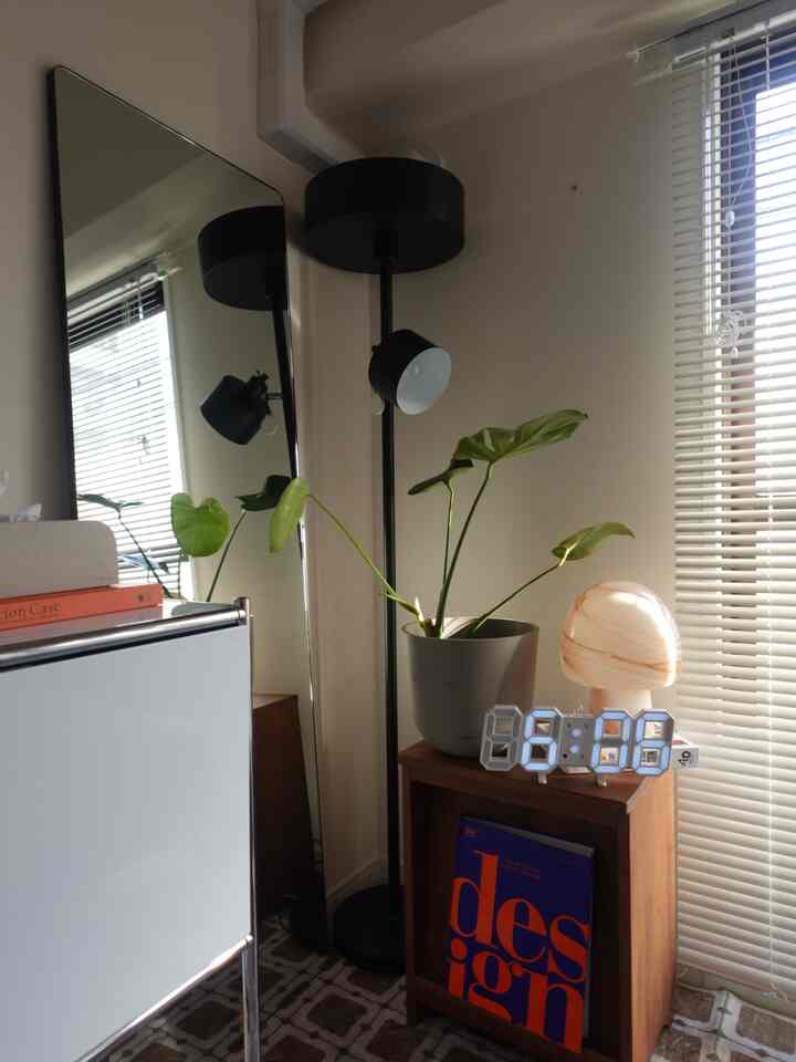 白い壁とブラウンの木目調サイドテーブルが配置されたモダンな空間、フロアランプと植物、デジタル時計が温かみのある雰囲気を演出