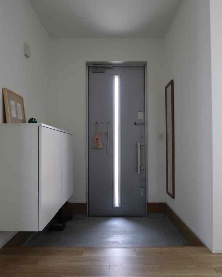 白とグレーの色調の玄関、浮いている靴箱が置かれ、壁に長い鏡が設置されたシンプルでコンパクトな空間