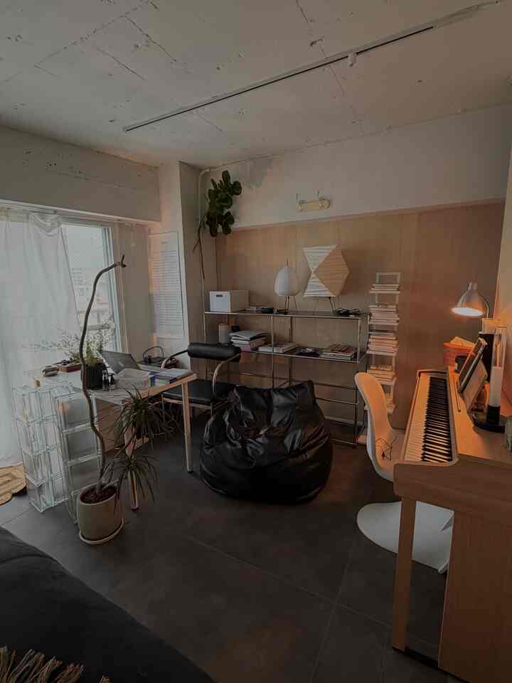 明るい木目調の壁と白い机、黒のビーズソファと電子ピアノが配置されたナチュラルモダンなホームオフィス兼書斎空間