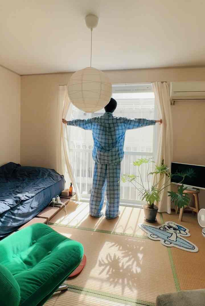 明るい白い壁と畳の床がある小さな一人暮らしの部屋、緑のアームチェアと植物が配置された落ち着く空間