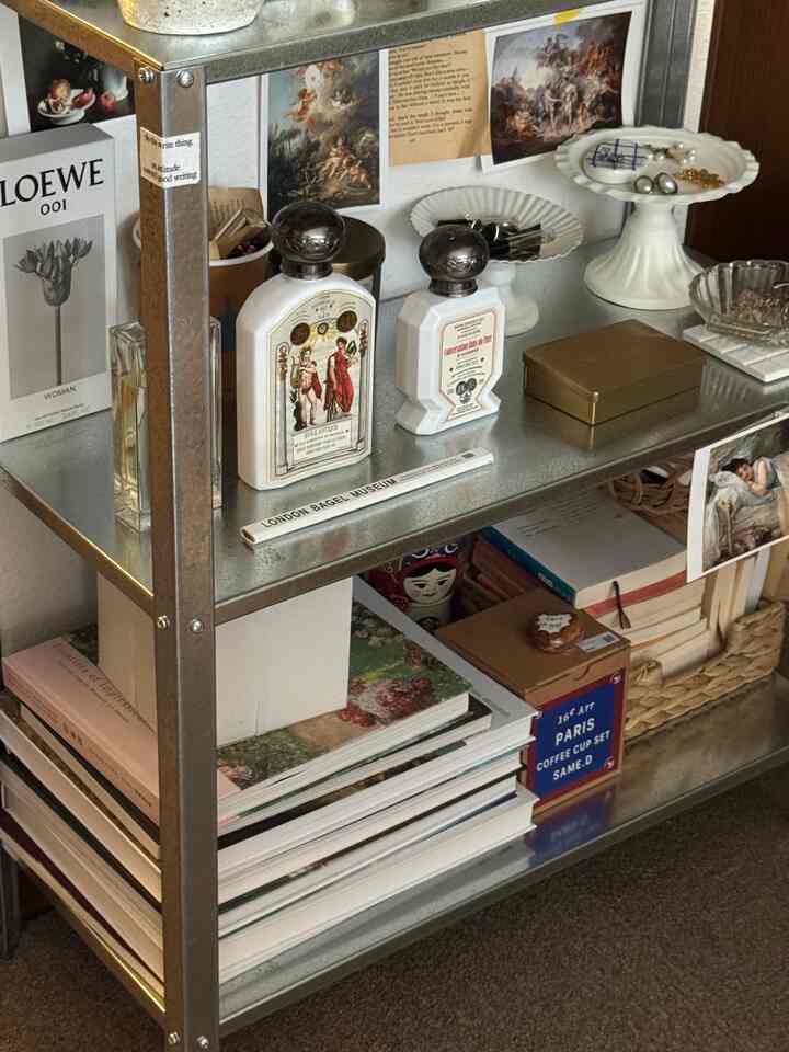シルバーの金属フレーム棚に本やゴールド・ホワイトの装飾品が整えられた雰囲気のある空間