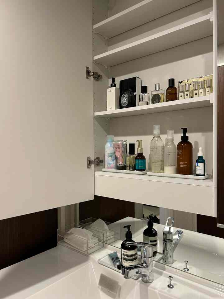 白を基調としたバスルームの空間、整理整頓された棚とトレイにさまざまな洗面用品が置かれたシンプルなインテリア