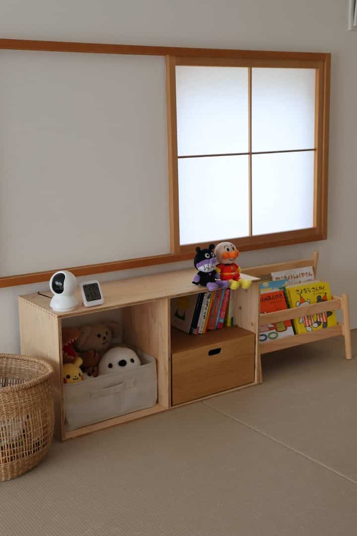 ナチュラルな木の色調とベージュの床が調和する子供部屋、子供のおもちゃと本棚が配置された落ち着いた空間