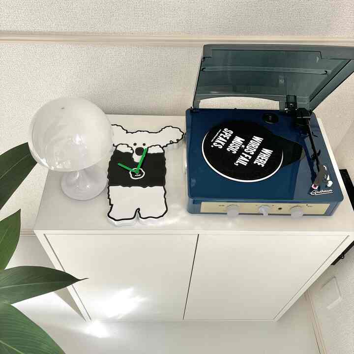 白とネイビーの色調のリビング、白いランプとクマ形の時計、ネイビーのレトロなレコードプレーヤーが配置された印象的なインテリア