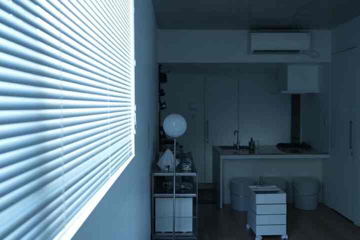 White and blue-toned studio kitchen space featuring blinds and minimal furniture with a simple, clean interior atmosphere