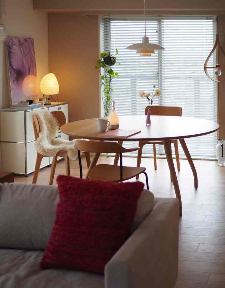 ベージュの壁と木目調の床のダイニングルーム、中央にラウンドテーブルと木製椅子、暖かい照明で雰囲気のあるインテリア。