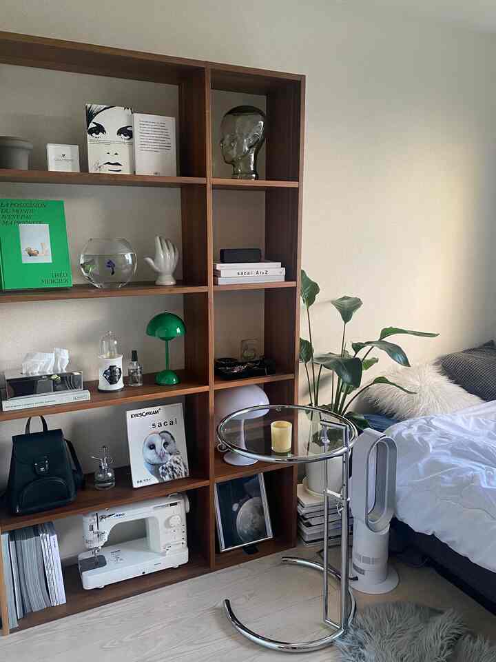 White and brown toned studio bedroom featuring wooden bookshelf and plant creating a cozy atmosphere