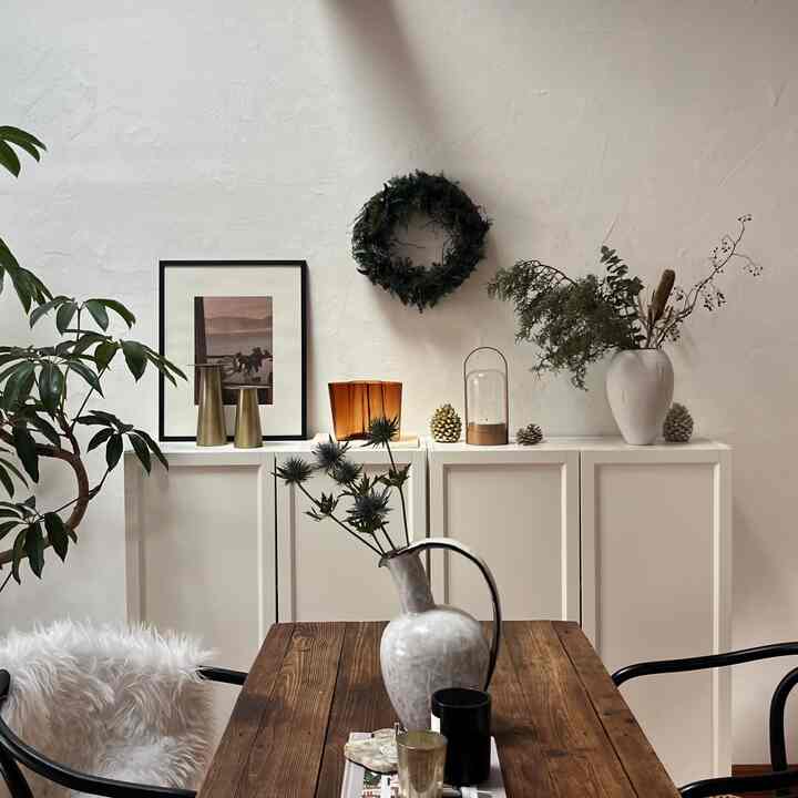 白い壁と家具の背景にナチュラルなリビング、木製ダイニングテーブルと花瓶、ガーランドが温かみのある雰囲気を醸し出す空間