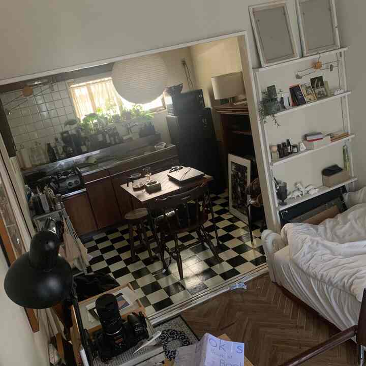 白と黒のチェッカーボードタイルの床、木目調家具、キッチンと寝室エリアがあるワンルームのアパートメント