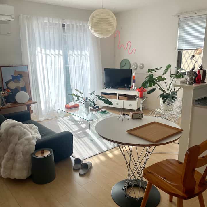 白とナチュラルカラーのリビング、ソファとガラスのコーヒーテーブル、グリーンプランツが配置された明るく居心地の良い空間