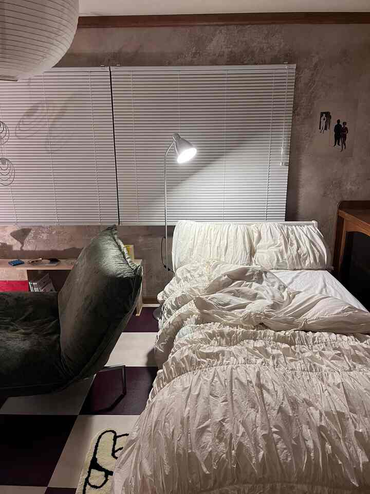 白い寝具とチェッカー柄の床が印象的な韓国風の寝室、間接照明と緑のソファが配置された落ち着いた空間