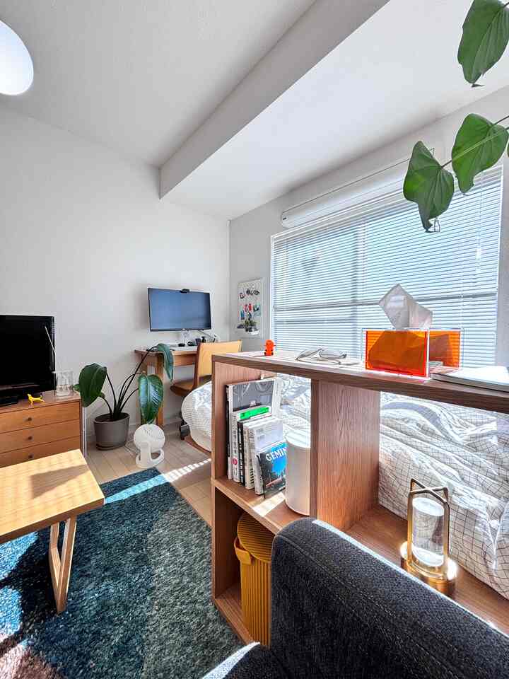 明るくナチュラルな色調の1人暮らし用1Kスタジオ、木製家具と青いラグ、ホームオフィスが配された清潔感のある空間